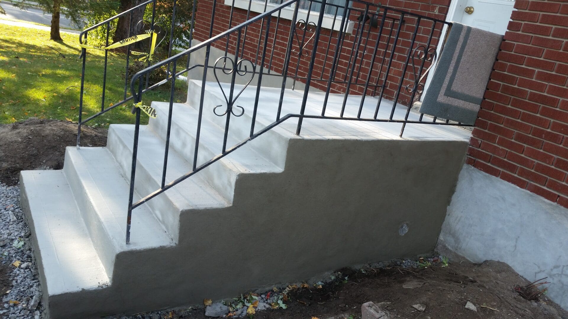 Parging the concrete stairs with black railings leading to a front door