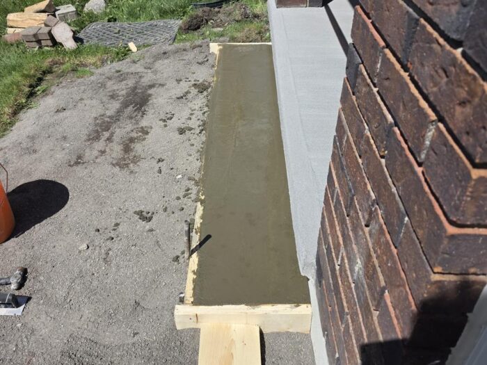 Freshly poured concrete strip against a brick foundation