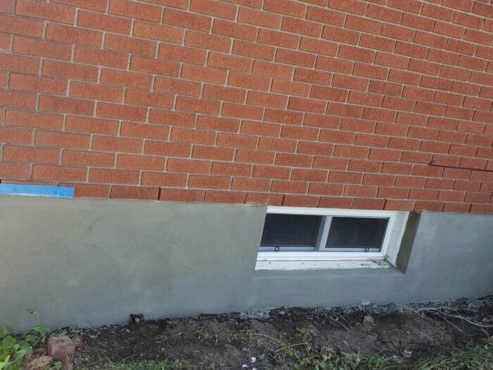 Parged foundation strip below the brick line and basement window