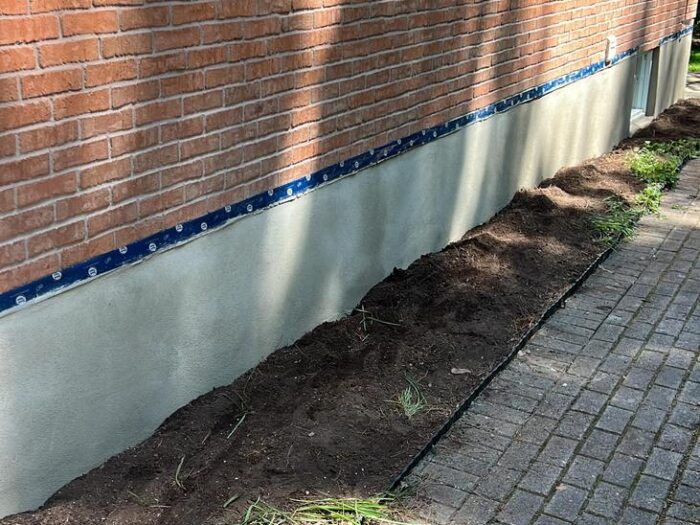 Parging in progress, masked to a clean line along the brick