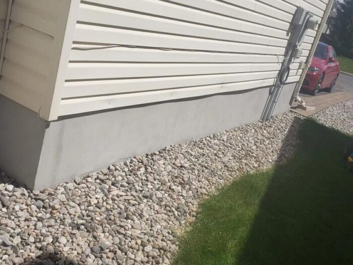 Parged foundation below vinyl siding and gravel
